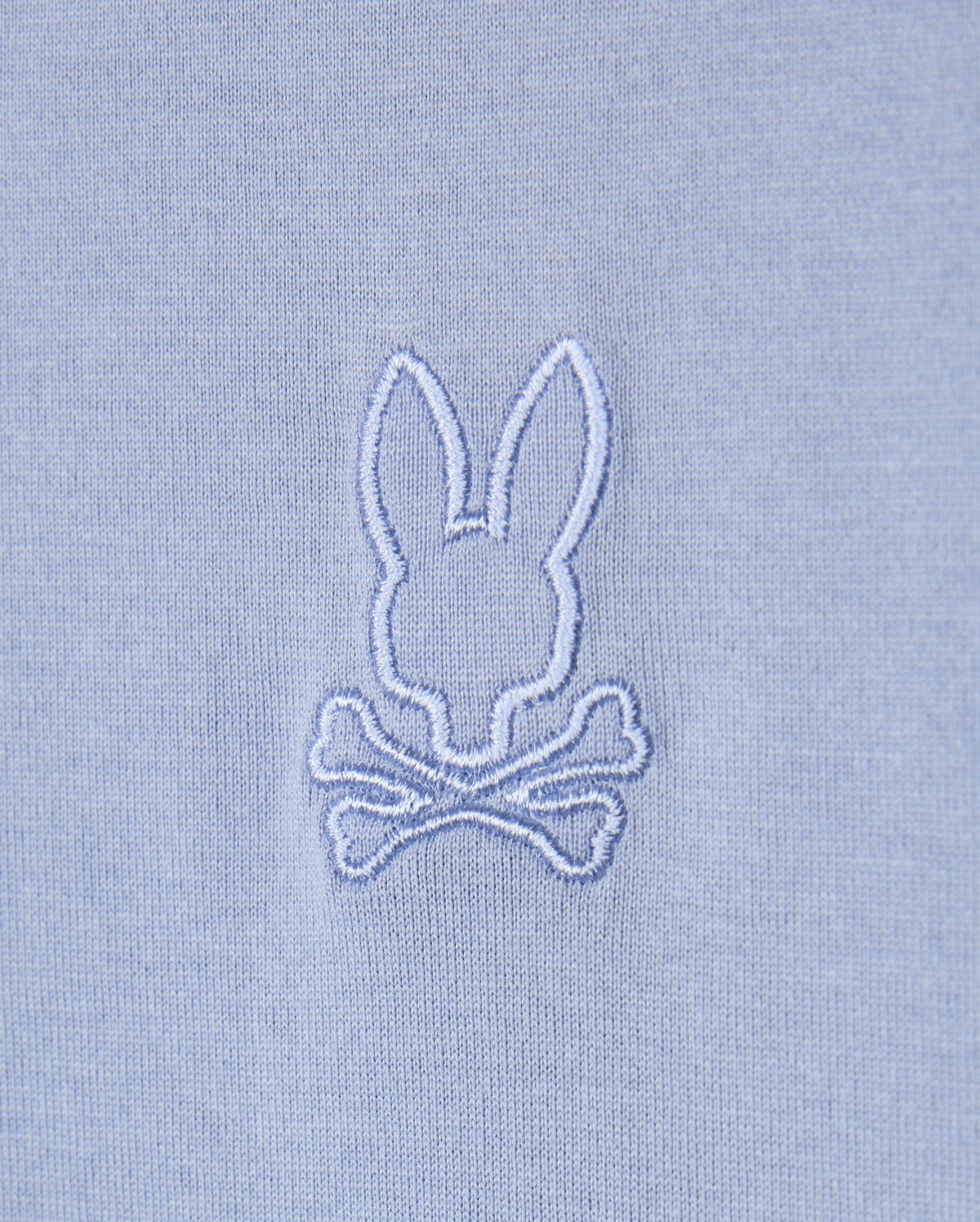 The Psycho Bunny MENS JAMES PREMIUM CREW NECK TEE - B6U952D200 features a light blue Pima cotton fabric with an embroidered design of a white bunny head above two crossed bones, creating a whimsical skull and crossbones motif that elevates this high-quality piece into the perfect embroidered tee.