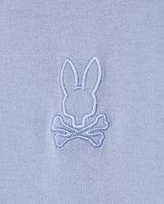 The Psycho Bunny MENS JAMES PREMIUM CREW NECK TEE - B6U952D200 features a light blue Pima cotton fabric with an embroidered design of a white bunny head above two crossed bones, creating a whimsical skull and crossbones motif that elevates this high-quality piece into the perfect embroidered tee.