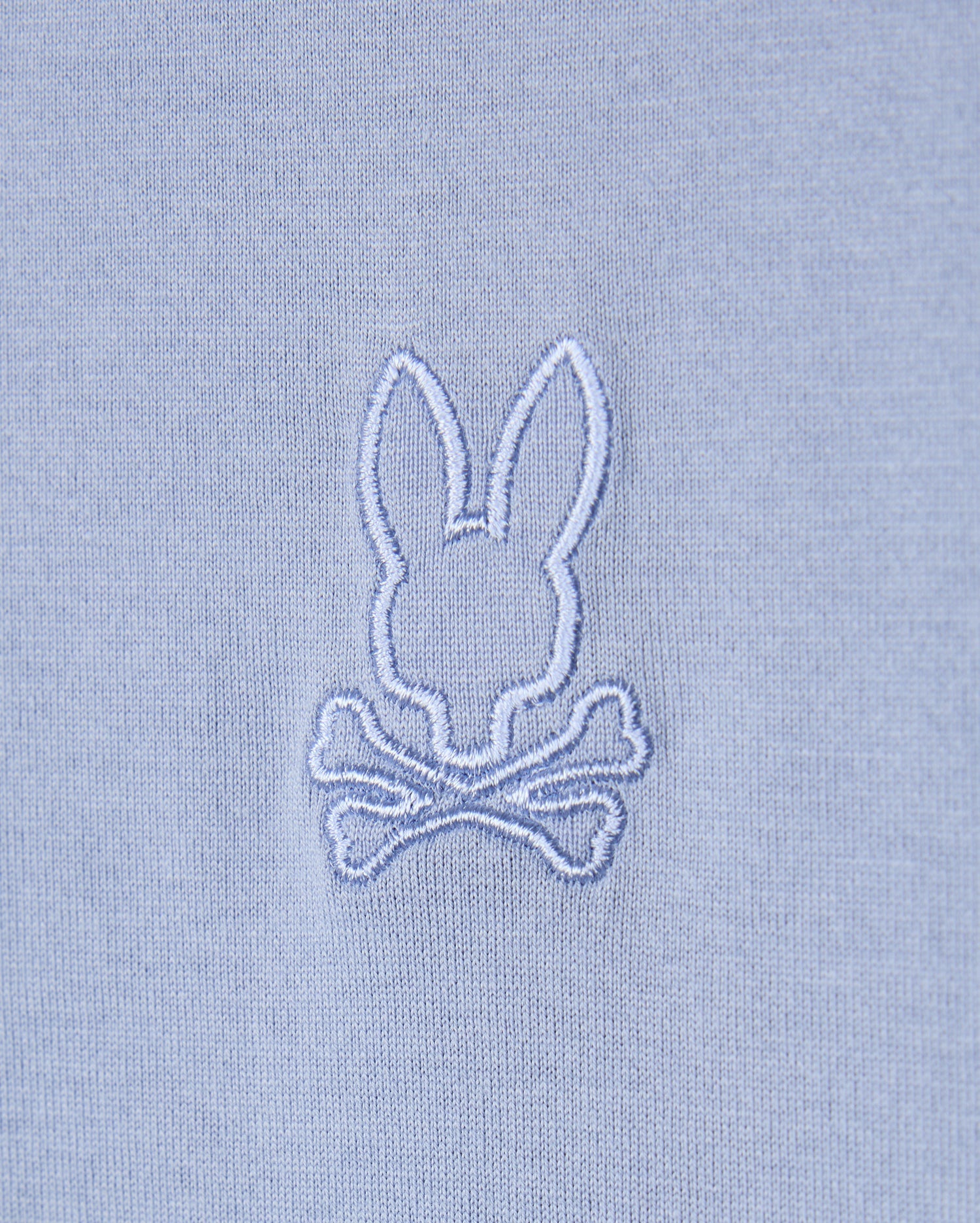 The Psycho Bunny MENS JAMES PREMIUM CREW NECK TEE - B6U952D200 features a light blue Pima cotton fabric with an embroidered design of a white bunny head above two crossed bones, creating a whimsical skull and crossbones motif that elevates this high-quality piece into the perfect embroidered tee.