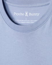 Close-up of a blue t-shirt highlighting the Psycho Bunny logo and brand name inside the neckline. The label proudly declares that the MENS JAMES PREMIUM CREW NECK TEE - B6U952D200 is crafted from 100% premium Pima cotton and manufactured in Peru, embodying the premium quality that defines this embroidered tee.