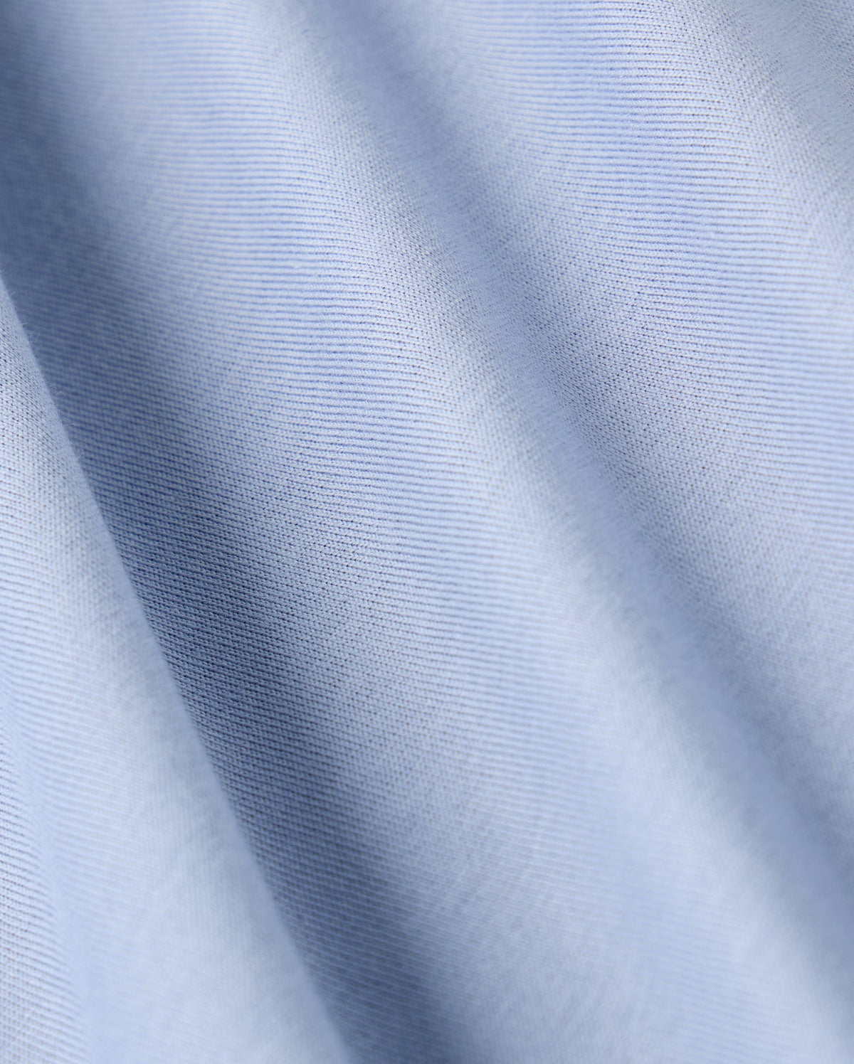 The Psycho Bunny MENS JAMES PREMIUM CREW NECK TEE (B6U952D200) features a close-up view of its premium quality light blue fabric, distinguished by fine diagonal lines. The smooth texture and subtle sheen highlight the softness typical of Pima cotton, with gentle waves and a consistent pattern throughout.