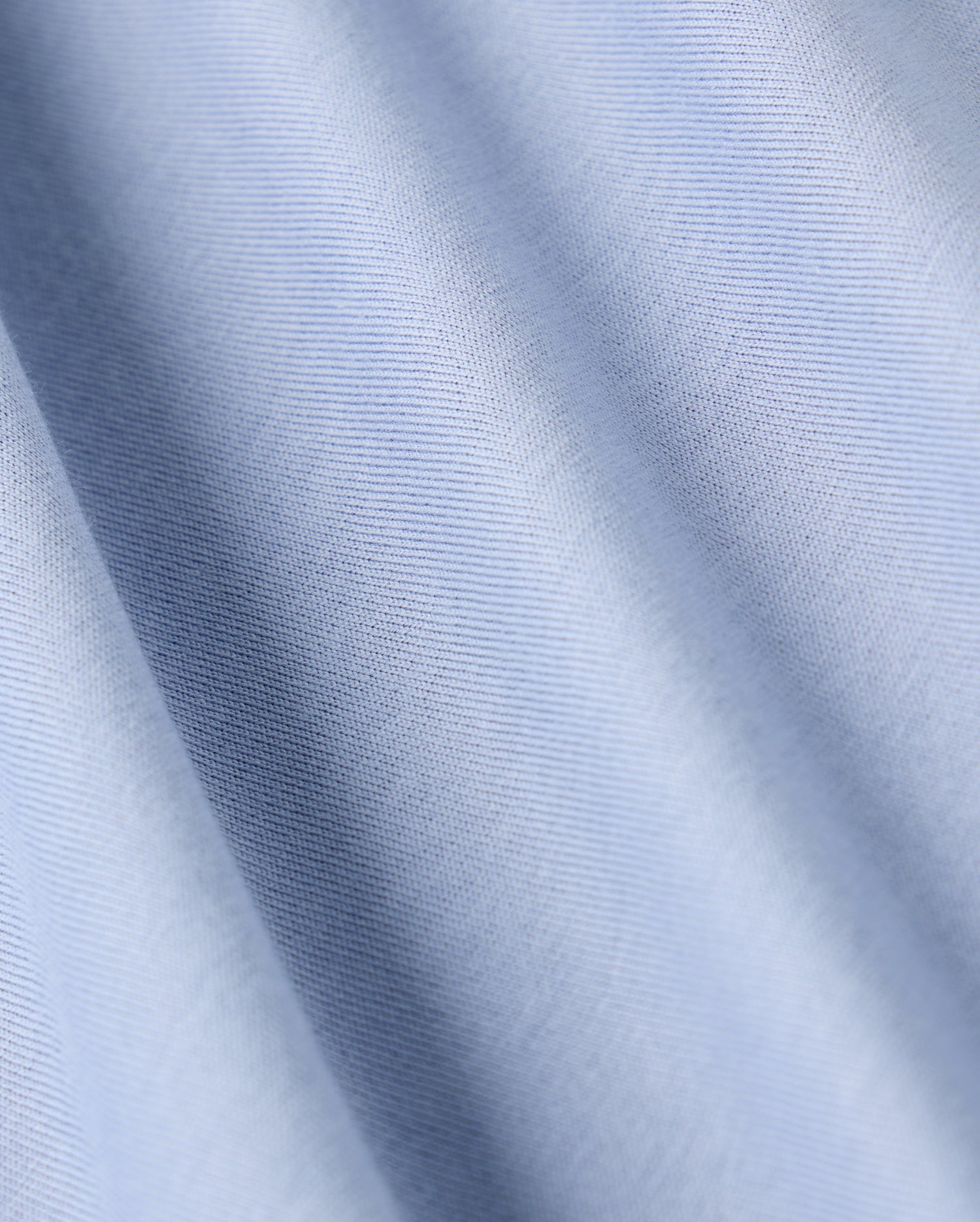 The Psycho Bunny MENS JAMES PREMIUM CREW NECK TEE (B6U952D200) features a close-up view of its premium quality light blue fabric, distinguished by fine diagonal lines. The smooth texture and subtle sheen highlight the softness typical of Pima cotton, with gentle waves and a consistent pattern throughout.