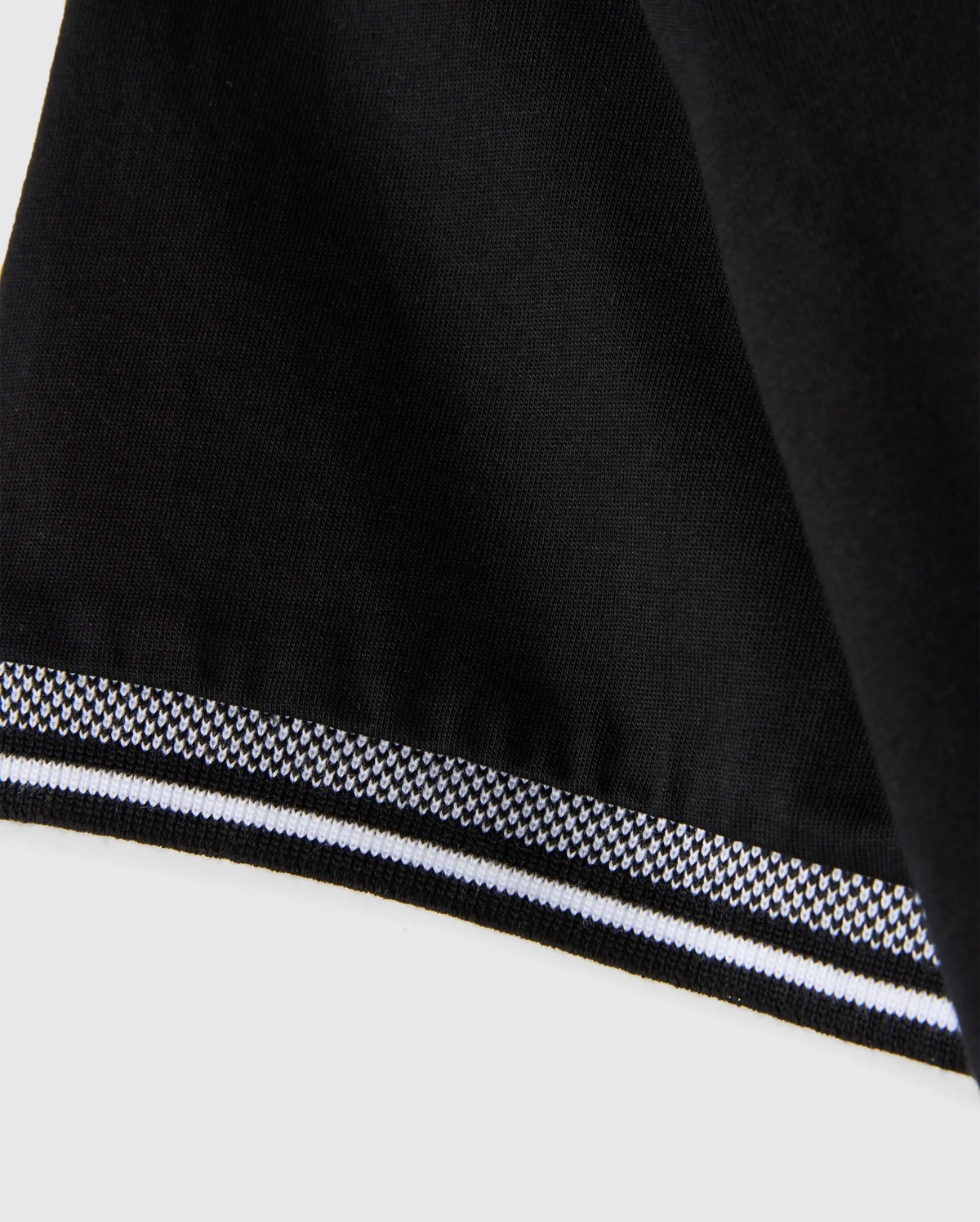 Close-up of a black Men's Malton Fashion Tee by Psycho Bunny, made from pima cotton, featuring a smooth texture and a stylish white and gray striped border at the edge. The border pattern is composed of small geometric shapes, making it an ideal addition to men's fashion tee collections.
