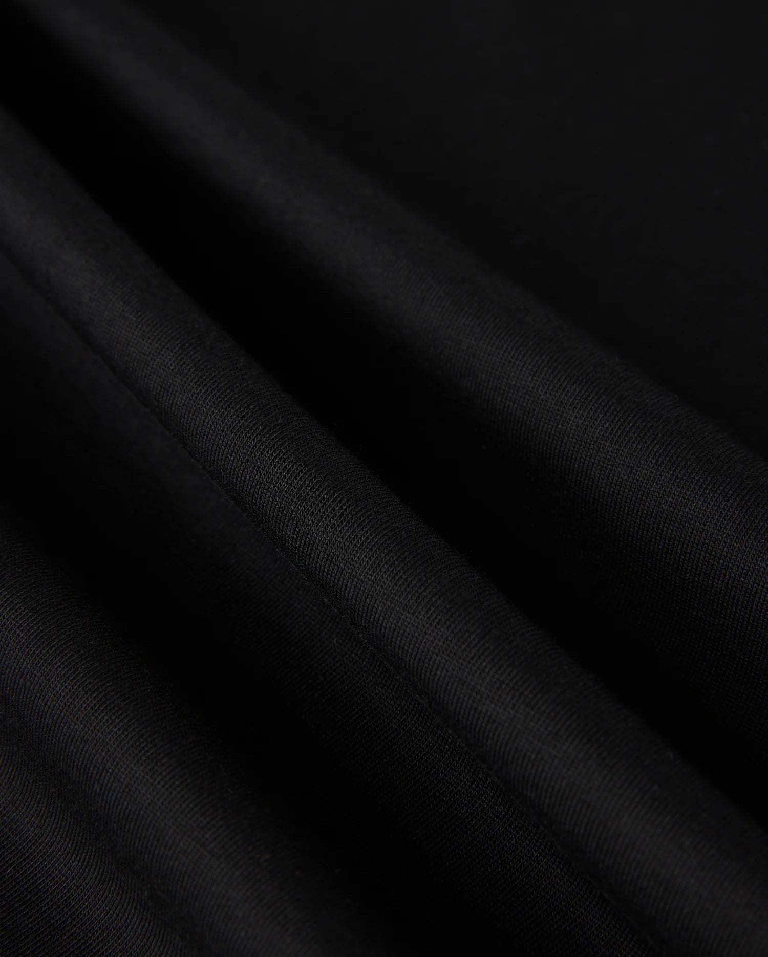 Close-up of the luxe, black fabric from the MENS MALTON FASHION TEE - B6U966D200 by Psycho Bunny, showcasing its smooth pima cotton with visible light reflections and folds, creating an elegant texture ideal for men's fashion.