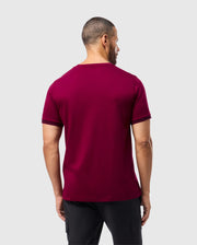 A man wearing a stylish Psycho Bunny MENS MALTON FASHION TEE - B6U966D200 in maroon, paired with black pants, stands with his back to the camera against a plain white background.