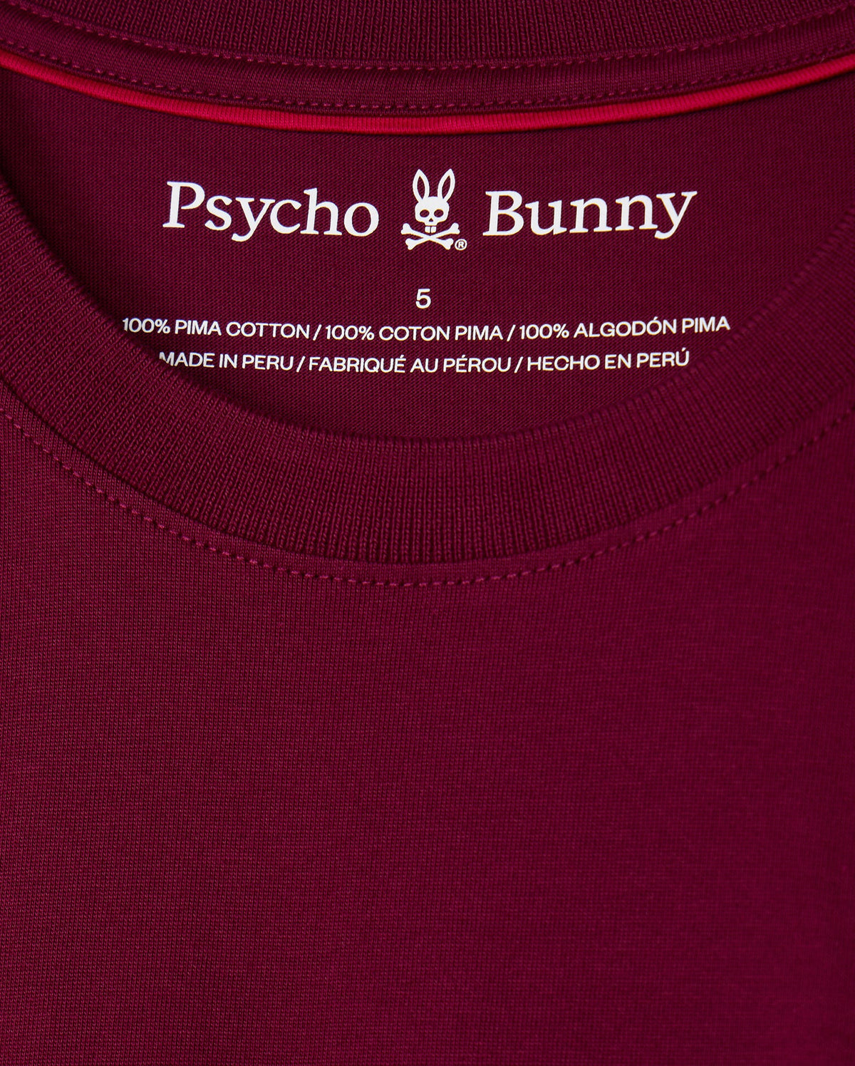 Close-up of the label on the maroon MENS MALTON FASHION TEE - B6U966D200 by Psycho Bunny, displaying size 5. The chic T-shirt label emphasizes "100% Pima Cotton" and notes that the shirt is "Made in Peru" in English, French, and Spanish.