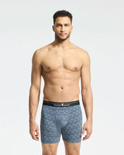 A man with short hair stands against a plain white background, wearing soft-knit patterned blue MENS 2 PACK BOXER BRIEF - B6V481F200 by Psycho Bunny. The briefs have a black waistband featuring the brand name, and his relaxed expression highlights their comfort and breathability.