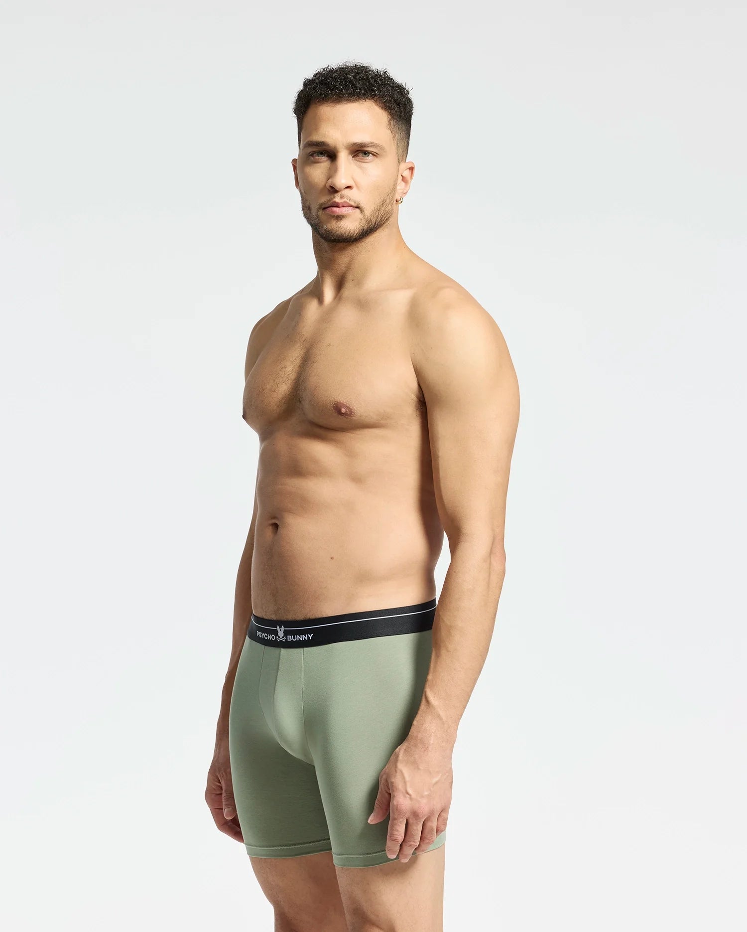 A man poses against a plain backdrop, wearing Psycho Bunny's MENS 2 PACK BOXER BRIEF - B6V481F200 in light green with a black waistband. Made from a Pima cotton-Modal blend, these stretchy briefs provide all-day comfort as he gazes forward, highlighting their perfect fit.