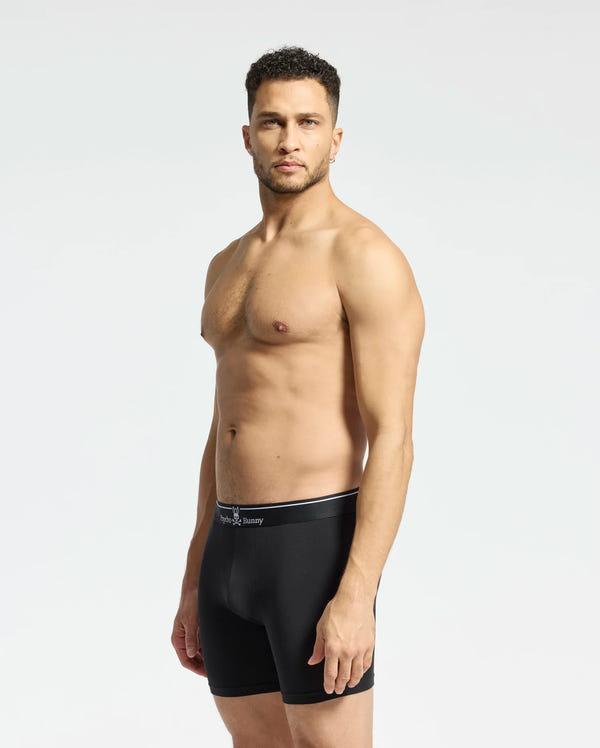 A man stands against a light gray background wearing the MENS SOLID KNIT 2 PACK BOXER BRIEF - B6V906ARCM by Psycho Bunny. He looks ahead with his arms at his sides, showcasing comfort and style in these ultrasoft modal-blend boxer briefs.