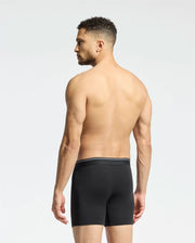 A man with short curly hair stands barefoot, facing away, wearing Psycho Bunny's MENS SOLID KNIT 2 PACK BOXER BRIEF - B6V906ARCM in black. The background is plain white.