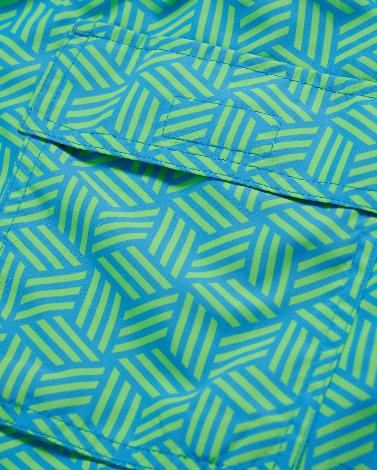 Close-up of a vibrant blue and green geometric-printed Psycho Bunny MENS JASPER LIGHTWEIGHT SWIM TRUNK - B6W168B2SW fabric, showing detailed stitching and texture.