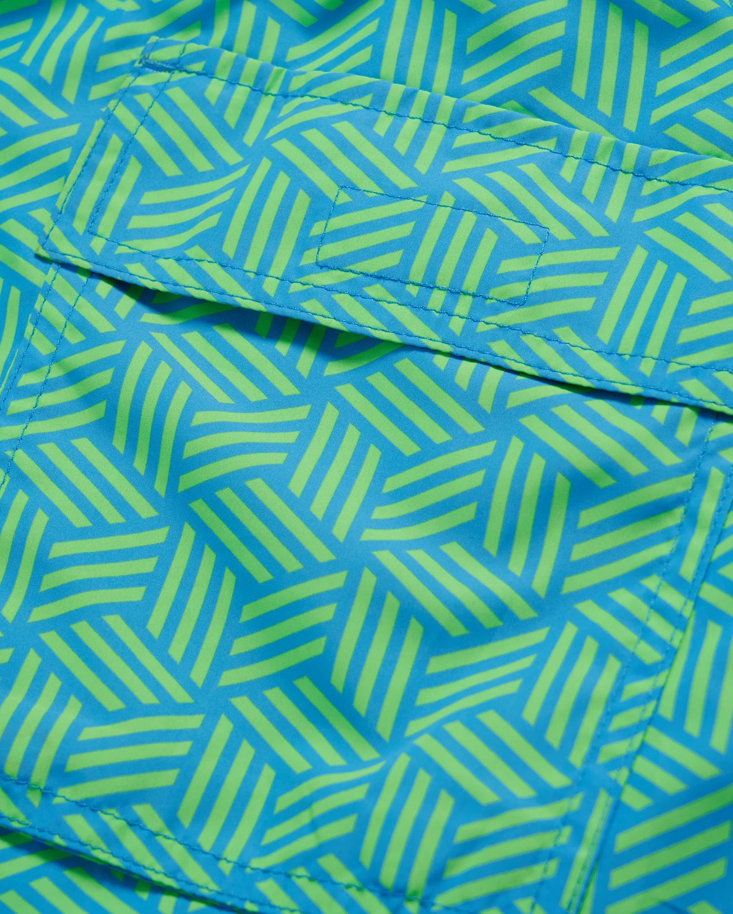 Close-up of a vibrant blue and green geometric-printed Psycho Bunny MENS JASPER LIGHTWEIGHT SWIM TRUNK - B6W168B2SW fabric, showing detailed stitching and texture.
