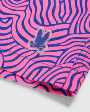 Close-up of a VERONA PRINT SWIM TRUNK - B6W172B2SW with a pink and blue wavy pattern. A small blue bunny skull and crossbones logo is visible on the quick-dry fabric from Psycho Bunny. The fabric appears to be folded, showcasing a stitched edge.