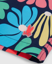 Close-up image of colorful floral patterned fabric featuring large, stylized flowers in blue, green, pink, and yellow. There is a red bunny with crossbones symbol attached to the fabric near the stitch line, reminiscent of stylish Psycho Bunny MENS MENTZ SWIM TRUNK - B6W320B2SW.
