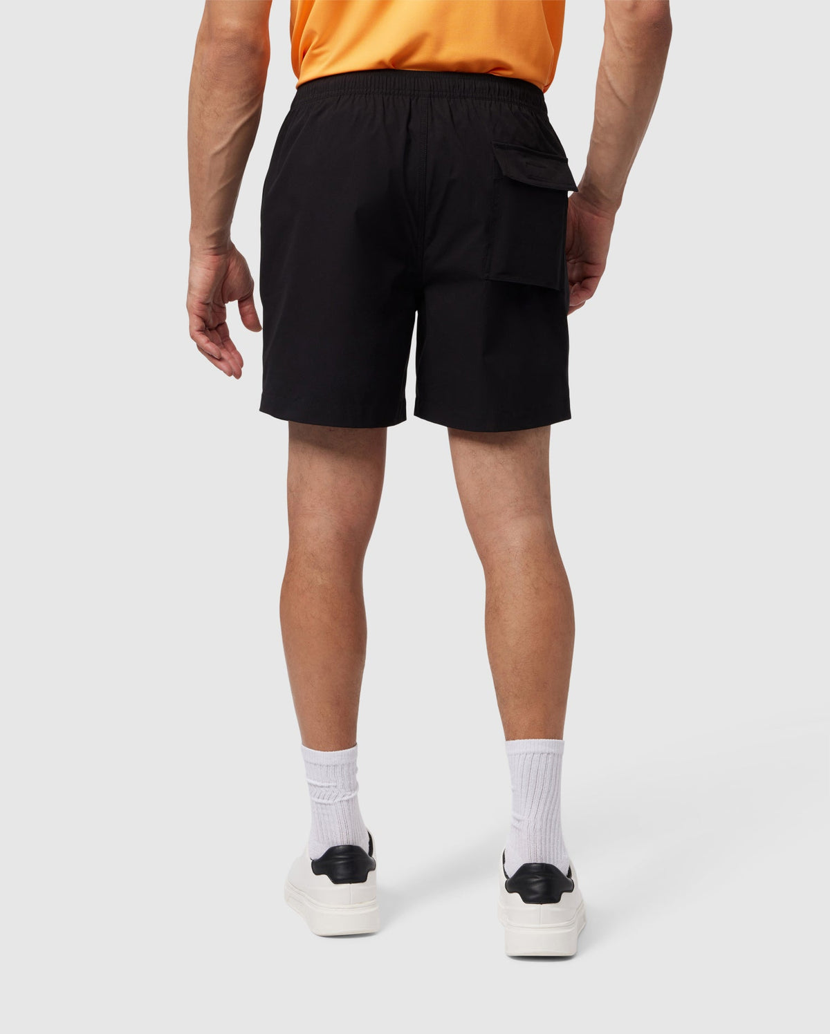 Rear view of a person from waist to ankles, wearing Psycho Bunny Malta swim trunks, white socks, and black and white sneakers, against a plain background.