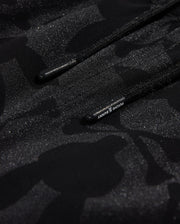 Close-up of a textured black fabric with a subtle camo pattern and glittery specks, featuring a drawstring with visible branding on the Psycho Bunny MENS MALTA HYDROCHROMIC SWIM TRUNK - B6W321B2SW.