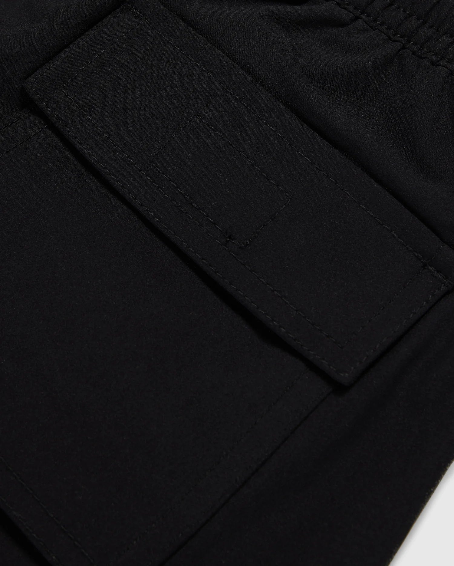 Close-up image of a black fabric texture with a detailed view of a sewn rectangular patch pocket on Psycho Bunny's MENS MALTA HYDROCHROMIC SWIM TRUNK - B6W321B2SW.