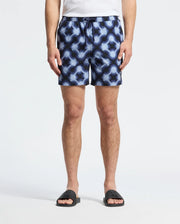 Wearing the Psycho Bunny MENS PAROS PRINTED SWIM TRUNK (B6W450F200), a person stands against a plain background. The drawstring waist ensures a perfect fit, complemented by black slide sandals. Their partially visible upper body adds mystery to this stylish ensemble.