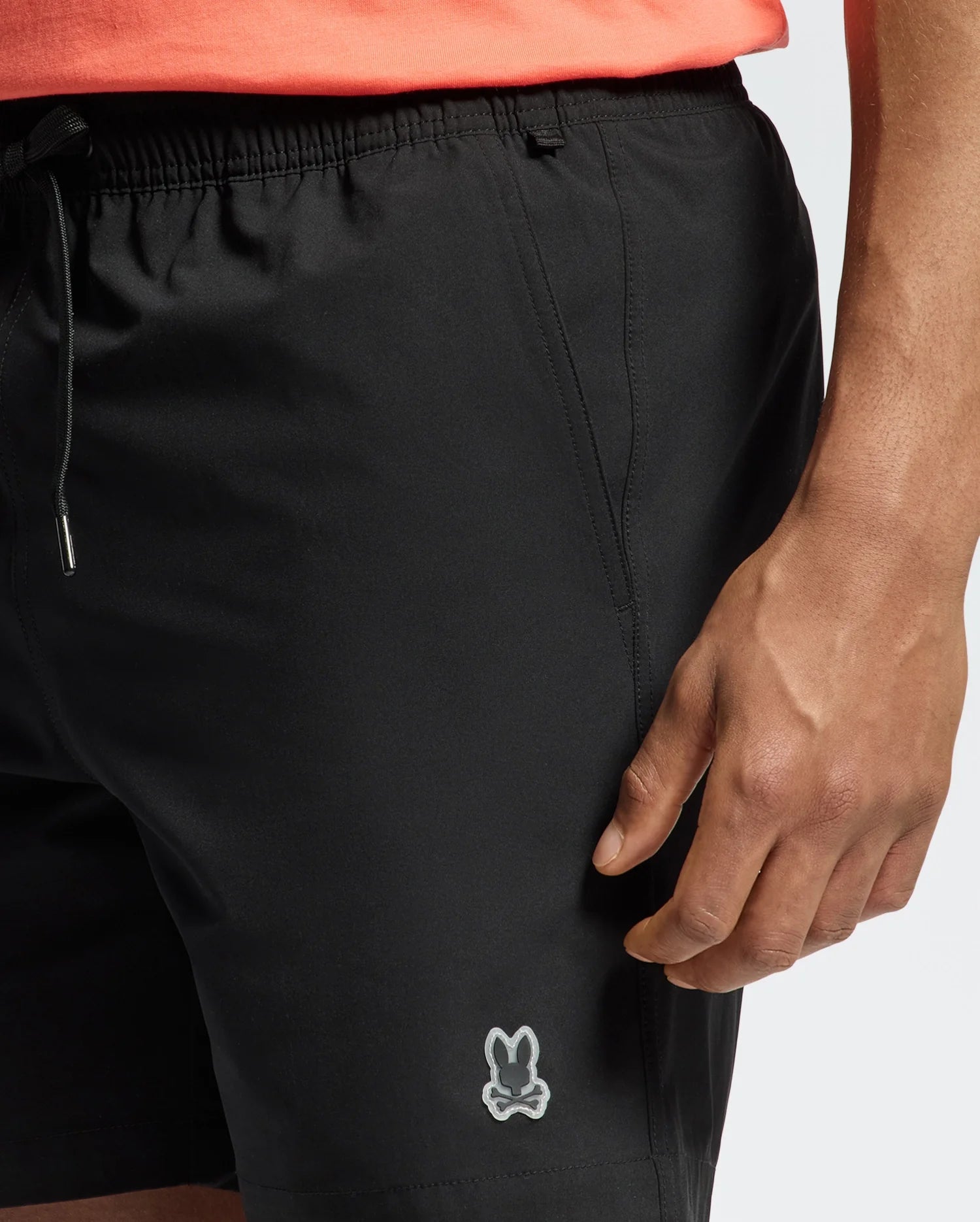 A person is wearing Psycho Bunny's MENS SAMOS HYDROCHROMIC PRINTED SWIM TRUNK, featuring a small logo near the hem, perfect for a pool party. The trunks have an elastic waistband and drawstring, paired with an unseen top in pink or coral.