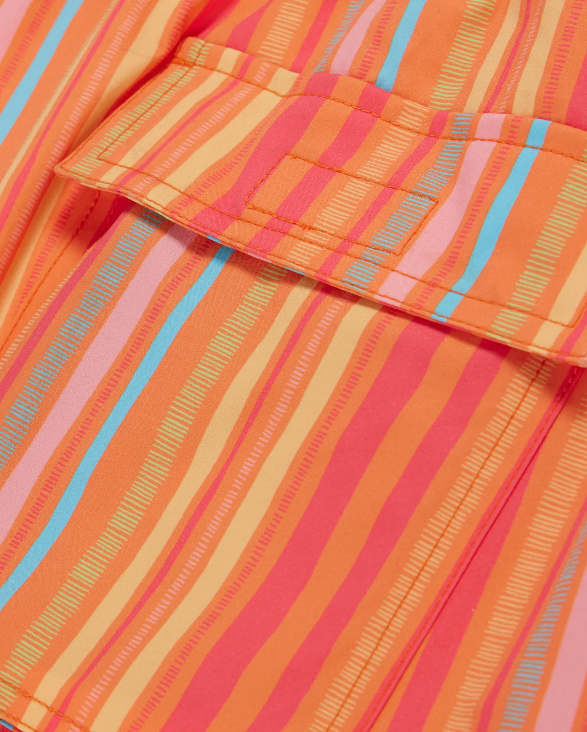 Close-up of a brightly colored fabric with a pattern of vertical stripes in various shades of orange, pink, and blue. The fabric appears to be part of MENS ANTON ALL OVER PRINT SWIM TRUNK - B6W542C200 by Psycho Bunny, with a visible pocket and stitching details.