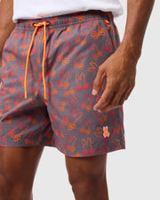 A person is shown from mid-torso to mid-thigh, wearing Psycho Bunny's MENS SHELDON ALL OVER PRINT SWIM TRUNK (Product Code: B6W588C200), featuring a gray base with orange and red bunny silhouettes. The swim trunks include an orange drawstring and are crafted from quick-dry fabric. The person is also wearing a white shirt against a plain white background.