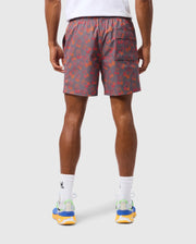 A person is wearing Psycho Bunny's MENS SHELDON ALL OVER PRINT SWIM TRUNK - B6W588C200, characterized by its gray design with an orange bunny pattern and a back pocket on the right side. Complementing the look are white socks with a black logo and colorful running shoes adorned with blue, green, and yellow accents.
