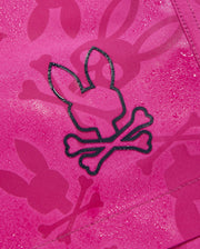 A close-up of a pink fabric with a bunny pattern featuring head silhouettes and crossbones. The water-repellent material has droplets on its surface, suggesting quick-drying Psycho Bunny MENS PARKER HYDROCHROMIC SWIM TRUNK - B6W646C200. Bunnies appear with crossed bones just below their heads, making for a unique design.