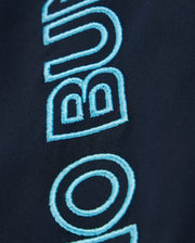 Close-up of a blue embroidered text on dark fabric, likely part of the MENS MELVIN SWIM TRUNK - B6W665C200 by Psycho Bunny. The bold, rounded font shows the visible letters "B U". The texture of the stitching is detailed, highlighting the craftsmanship. These Melvin swim trunks feature a quick-dry outer shell and a drawstring stretch waistband for comfort.
