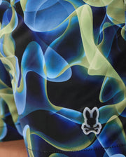 Close-up image of colorful, abstract-patterned fabric in shades of blue, green, and black. The fabric belongs to a Psycho Bunny Men's Goldcreek All Over Print Swim Trunk (B6W672C200) and features a small, white embroidered patch with a bunny head silhouette near the edge.