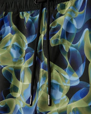Detailed look at the MENS GOLDCREEK ALL OVER PRINT SWIM TRUNK - B6W672C200 by Psycho Bunny, showcasing a vibrant abstract pattern with swirling shapes in shades of green, blue, and black. The swim trunks feature black drawstrings with small metallic end caps for added style.