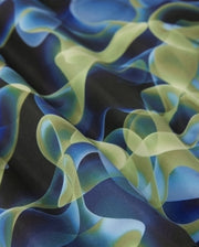 A close-up view of the Psycho Bunny MENS GOLDCREEK ALL OVER PRINT SWIM TRUNK - B6W672C200, featuring an abstract fabric design with smooth, flowing, intertwining shapes in shades of blue, green, and black. The patterns create a sense of movement and fluidity, resembling waves or translucent ribbons—perfect for a stylish and comfortable swim piece.