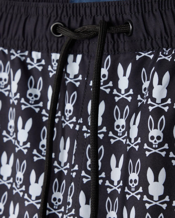 Close-up of the Psycho Bunny MENS TILDEN PRINT SWIM TRUNK - B6W729D200, showcasing a distinctive design where bunny heads replace skulls in a contrasting print. This black garment features white patterns and black drawstrings at the center, made with a quick-dry membrane for optimal performance.