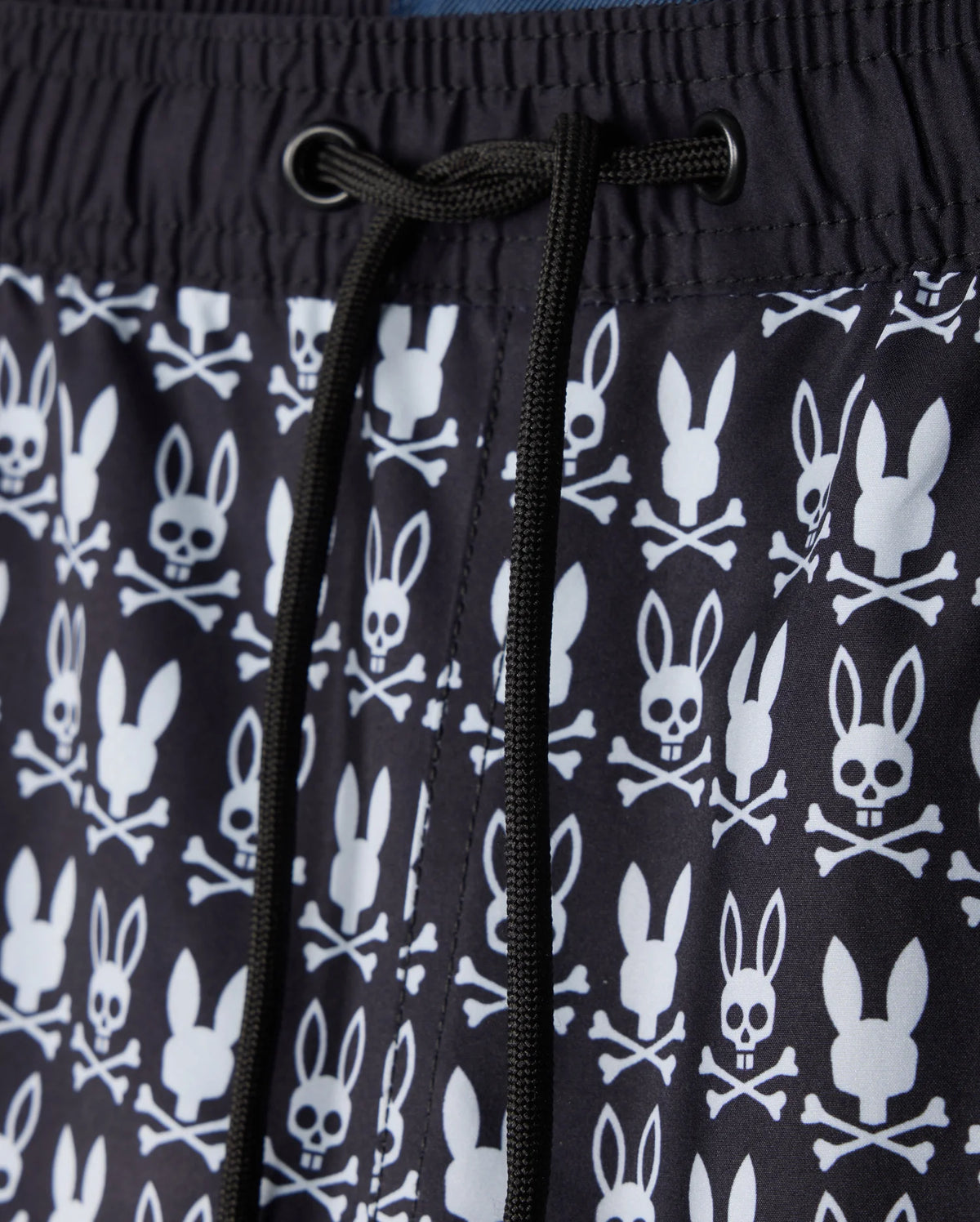 Close-up of the Psycho Bunny MENS TILDEN PRINT SWIM TRUNK - B6W729D200, showcasing a distinctive design where bunny heads replace skulls in a contrasting print. This black garment features white patterns and black drawstrings at the center, made with a quick-dry membrane for optimal performance.