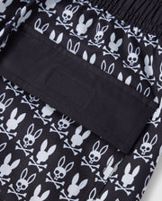 A close-up of the Psycho Bunny MENS TILDEN PRINT SWIM TRUNK - B6W729D200 featuring a contrast bunny print with white cartoon-style bunny skulls and crossbones. The image focuses on a back pocket with a flap secured by Velcro. The elastic waistband makes these swim trunks perfect for any casual or beach setting.