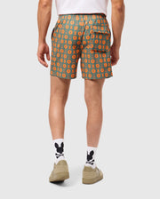 Reconstructed Sentence: Rear view of a person wearing green and orange patterned Psycho Bunny MENS ARNOLD PRINT SWIM TRUNK - B6W820D200 with "MO" initials, a white t-shirt, white socks featuring black cartoon-style characters, and beige slip-on shoes. The quick-dry material shorts have a buttoned pocket on the right side and are knee-length.