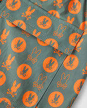 Close-up of the green fabric with an orange bunny-head-and-crossbones pattern featured on the MENS ARNOLD PRINT SWIM TRUNK - B6W820D200 by Psycho Bunny. Orange circles display the same design. A pocket with a flap highlights the fabric's print and stitching details. Ideal for these swim trunks, this quick-dry material includes a comfortable stretch mesh lining perfect for swimming and lounging.