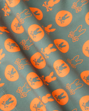 The MENS ARNOLD PRINT SWIM TRUNK - B6W820D200 by Psycho Bunny features a repetitive pattern of orange circles each containing a silhouette of a rabbit, set against a green background. The slightly wrinkled quick-dry material lends dynamic texture to the overall design, making these swim trunks an ideal choice.