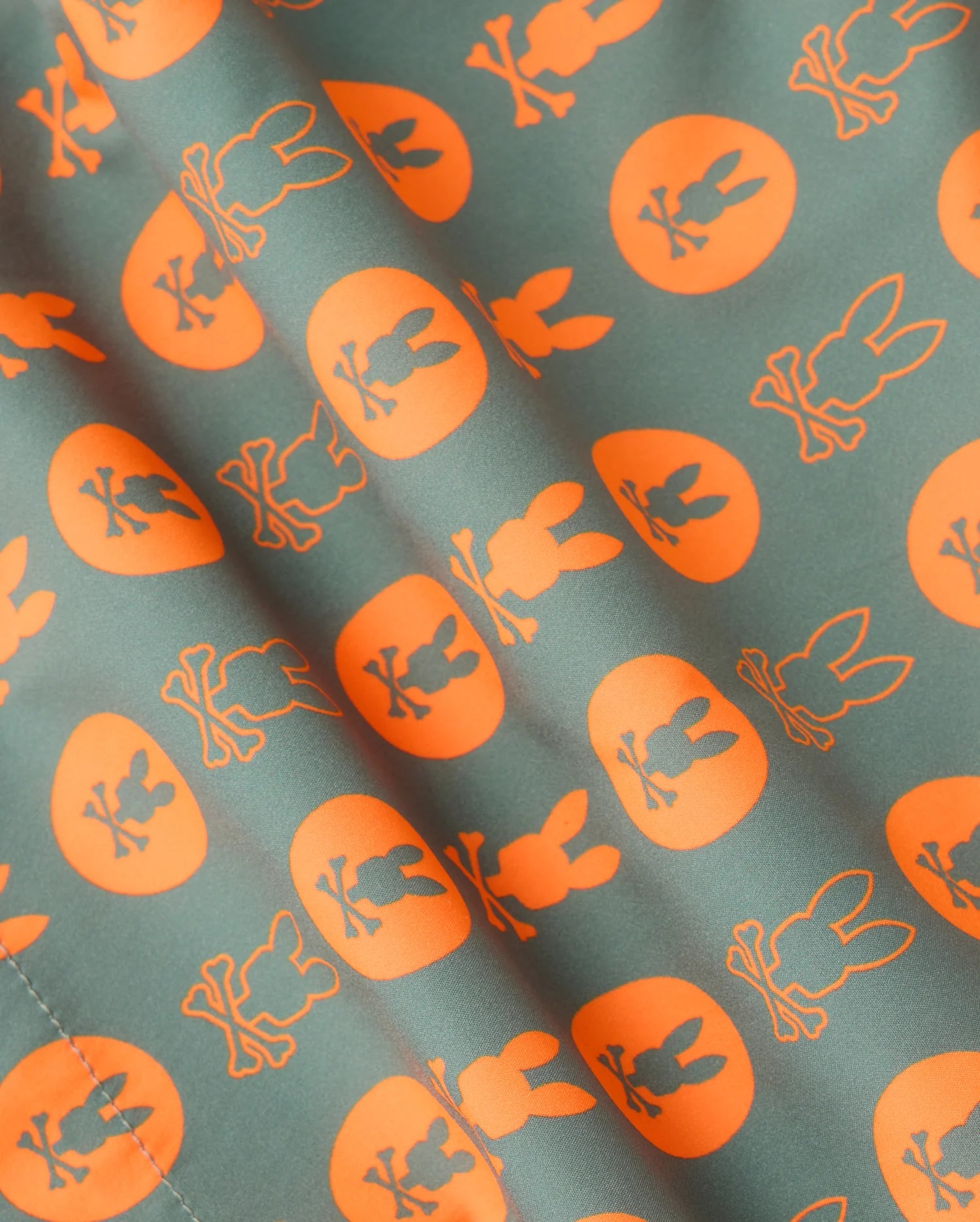 The MENS ARNOLD PRINT SWIM TRUNK - B6W820D200 by Psycho Bunny features a repetitive pattern of orange circles each containing a silhouette of a rabbit, set against a green background. The slightly wrinkled quick-dry material lends dynamic texture to the overall design, making these swim trunks an ideal choice.