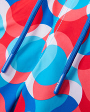 Close-up of a vibrant MENS WALTER LIGHTWEIGHT PRINT SWIM TRUNK - B6W863D200 from Psycho Bunny, featuring a wavy, overlapping circle pattern in shades of blue, red, and white. Made from 100% polyester, the fabric includes blue drawstrings with textured detailing and the text "Musto" written on them. The image highlights the colorful design.