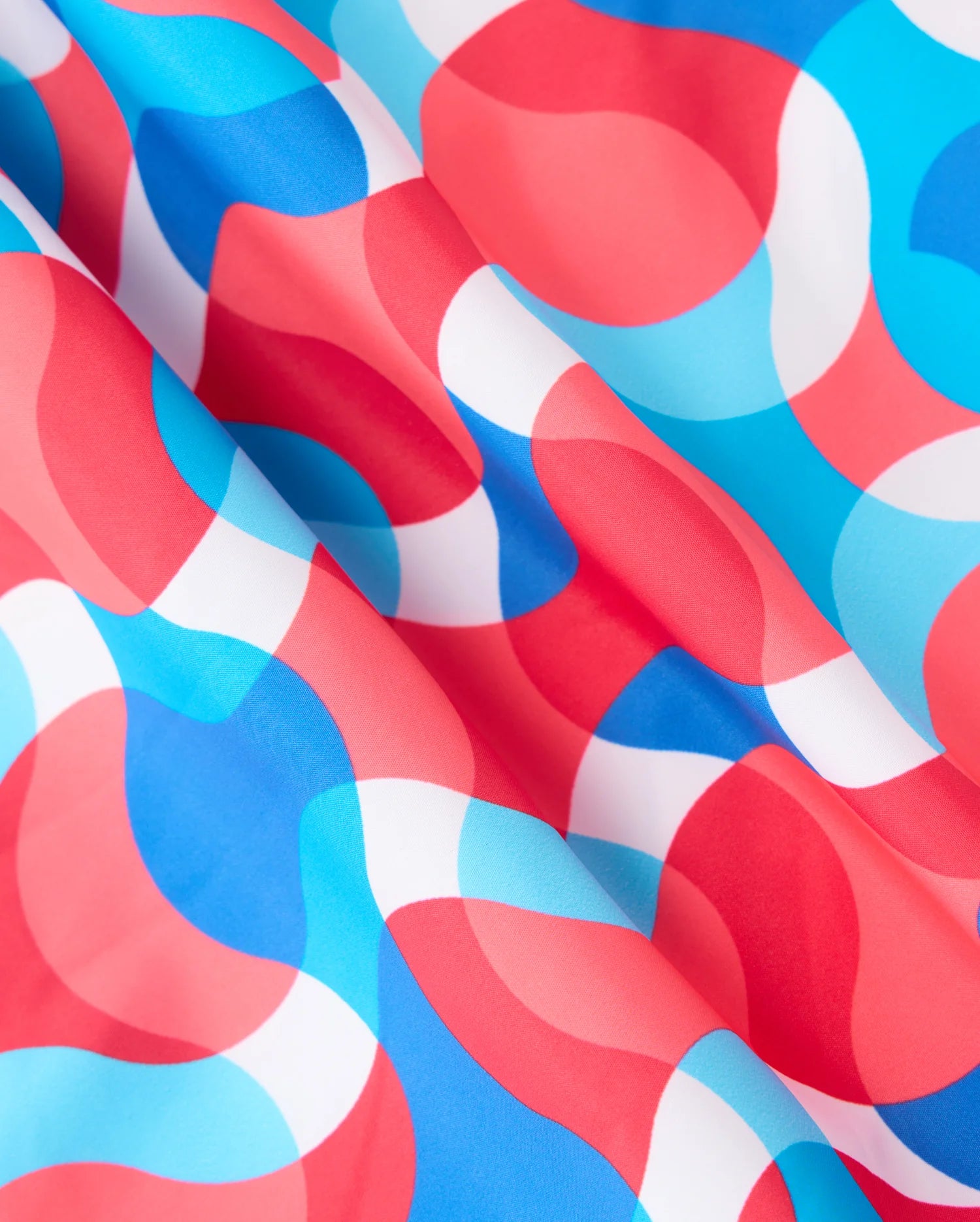 A close-up of wavy, abstract patterns in vibrant red, blue, and white colors on a 100% polyester fabric. The intertwining shades create a dynamic and fluid design that characterizes the MENS WALTER LIGHTWEIGHT PRINT SWIM TRUNK - B6W863D200 by Psycho Bunny. The slightly wrinkled texture adds depth to the visually engaging pattern.