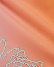 Close-up of silky orange fabric with a smooth texture, featuring a pale blue abstract design in one corner. The fabric has a light sheen, giving it a slightly reflective surface. This HD-printed bunny pattern adds charm, and the material is quick-drying—ideal for the Psycho Bunny MENS WINTON PRINTED SWIM TRUNK - B6W915A2PO.