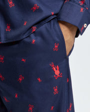 A close-up of a person wearing the Psycho Bunny Men's All Over Print Flannel Pajama Set (B6X343E200) features red embroidered rabbit designs. Their hand rests casually in the pocket, emphasizing the soft flannel texture. The playful motif adorns the cozy cotton flannel sleepwear, adding charm to this comfortable set.