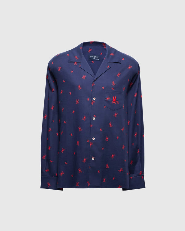 The MENS ALL OVER PRINT FLANNEL PAJAMA SET - B6X343E200 from Psycho Bunny is a stylish navy blue button-up shirt adorned with a vibrant red palm tree print on a light gray background. Designed for maximum comfort, it resembles a soft flannel sleep set and features long sleeves and a chest pocket.