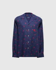The MENS ALL OVER PRINT FLANNEL PAJAMA SET - B6X343E200 from Psycho Bunny is a stylish navy blue button-up shirt adorned with a vibrant red palm tree print on a light gray background. Designed for maximum comfort, it resembles a soft flannel sleep set and features long sleeves and a chest pocket.