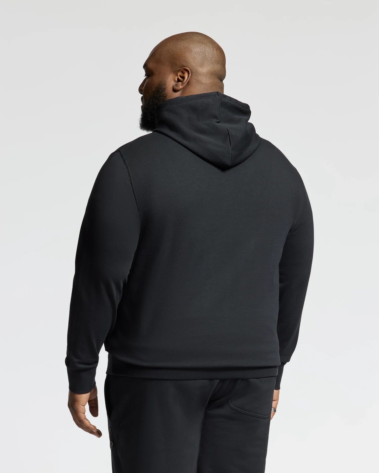 A man wearing a Psycho Bunny BIG AND TALL ALEXANDER HOODIE - B9H154E200 in black, along with matching pants, is shown from the back against a plain background.