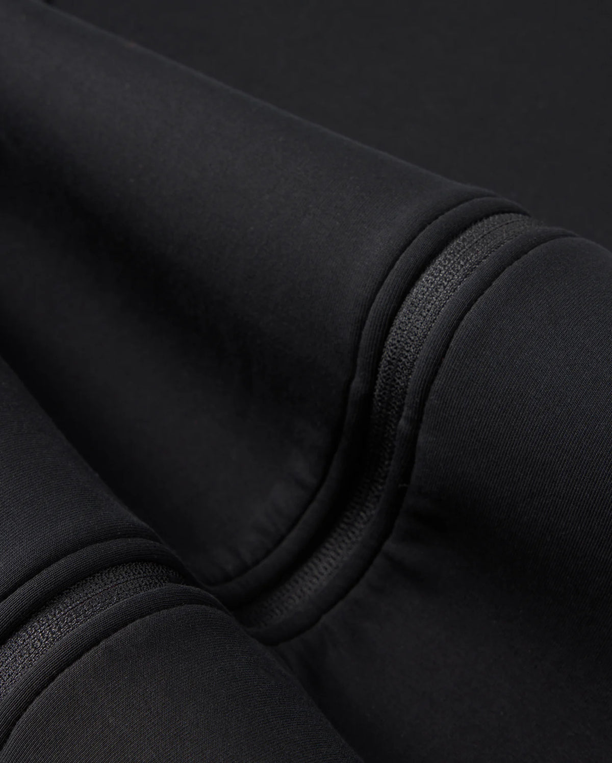 A close-up of the folded Psycho Bunny BIG AND TALL TRAVIS TRACK JACKET - B9J142D200 shows black cotton-blend fabric with visible seams and stitching. The surface appears soft and smooth, with subtle shadows enhanced by silicone heat transfer techniques.