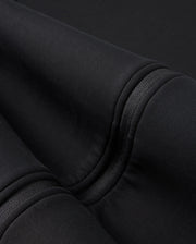A close-up of the folded Psycho Bunny BIG AND TALL TRAVIS TRACK JACKET - B9J142D200 shows black cotton-blend fabric with visible seams and stitching. The surface appears soft and smooth, with subtle shadows enhanced by silicone heat transfer techniques.