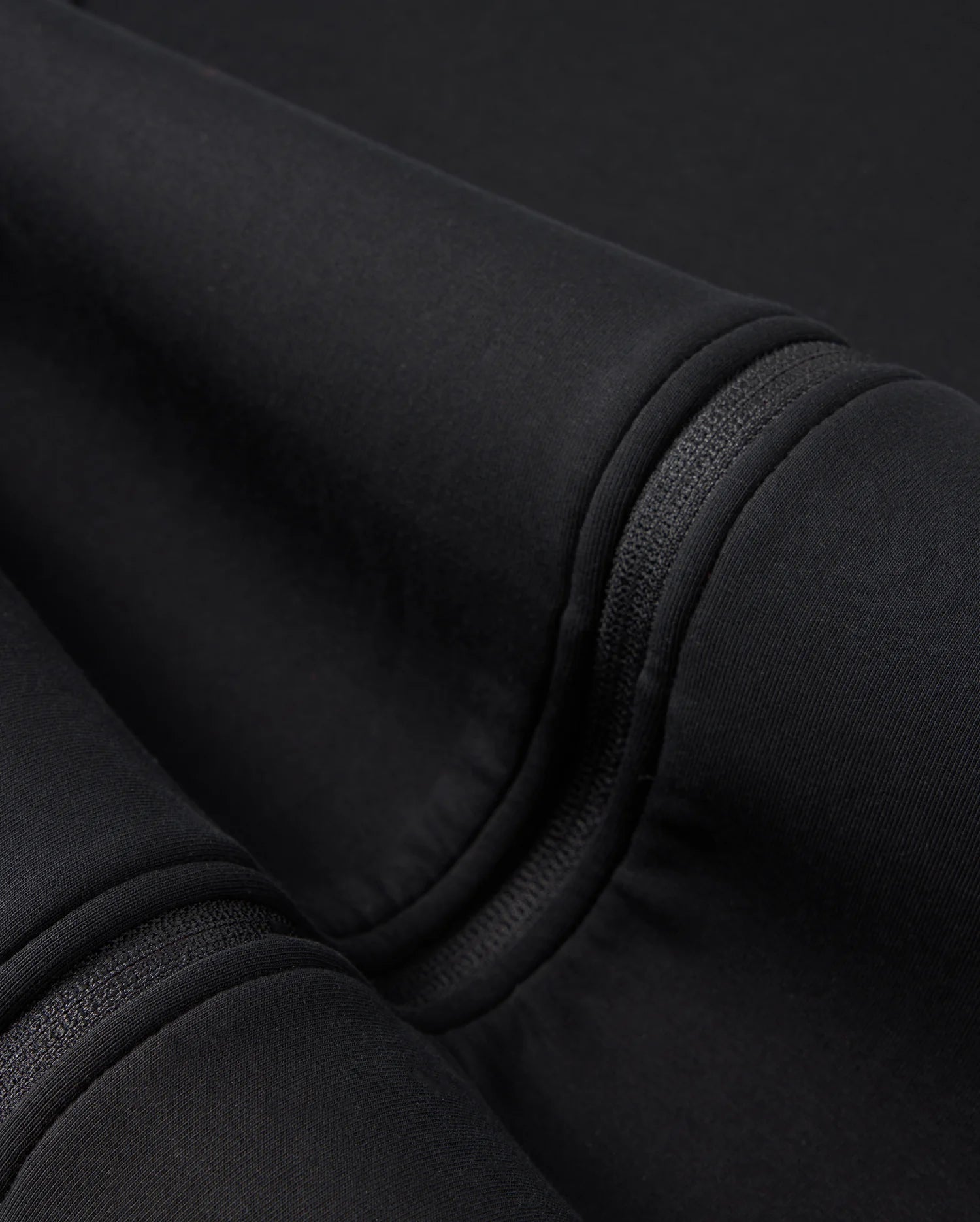 A close-up of the folded Psycho Bunny BIG AND TALL TRAVIS TRACK JACKET - B9J142D200 shows black cotton-blend fabric with visible seams and stitching. The surface appears soft and smooth, with subtle shadows enhanced by silicone heat transfer techniques.