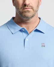 A bearded person is wearing a light blue Psycho Bunny BIG AND TALL CLASSIC PIQUE POLO, featuring a small pink bunny with crossbones logo on the chest, with focus on the upper torso and this stylish symbol.