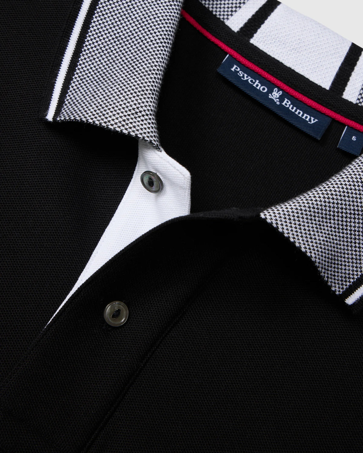 Close-up of the Psycho Bunny Big and Tall Malton Pique Polo Shirt in black, featuring a contrasting white and black checkered collar, sleek black button placket, and the iconic "Psycho Bunny" logo tag inside with a touch of red on the inner collar.